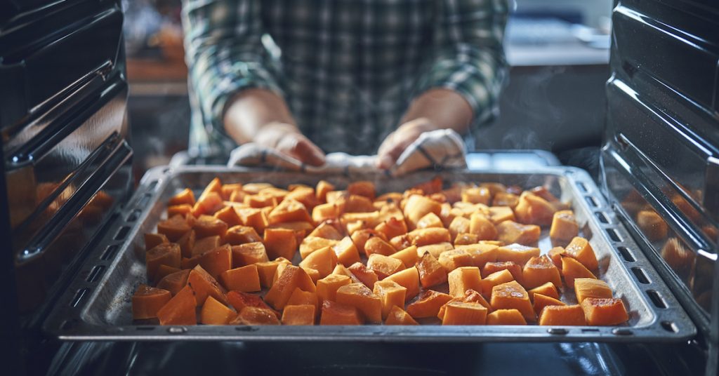 Picture of someone pulling pumpkin pieces out of the oven.